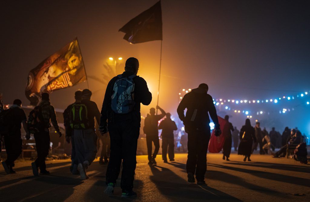 Pilgrims walking at night under string lights and flags